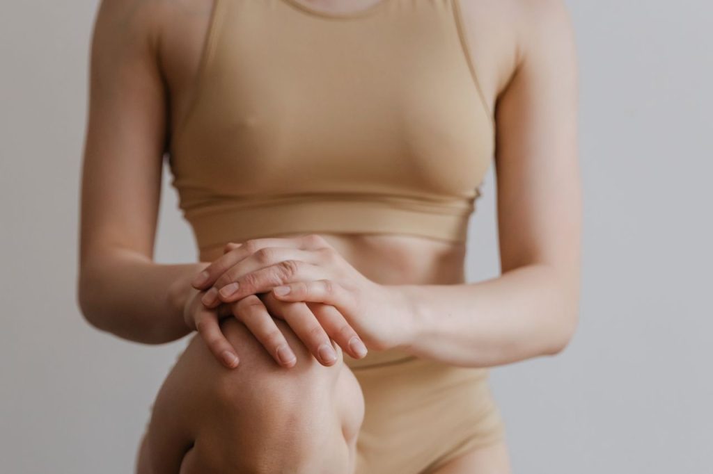 A young woman wearing beige sportswear kneeling indoors, focusing on fitness and mindfulness.
